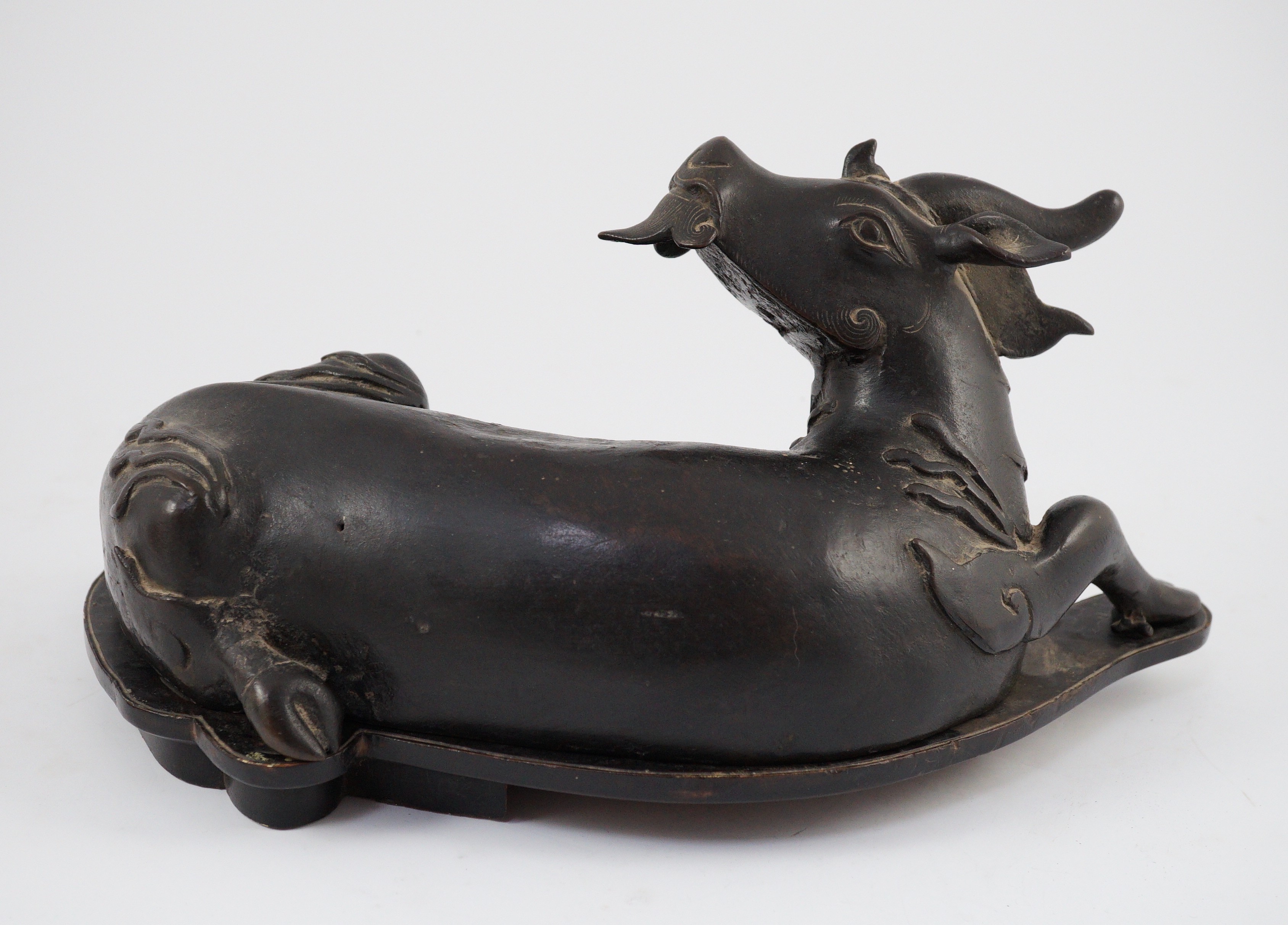 A Chinese bronze figure of a recumbent qilin, late Ming dynasty, 36cm long, old repairs and later base panel, wood stand